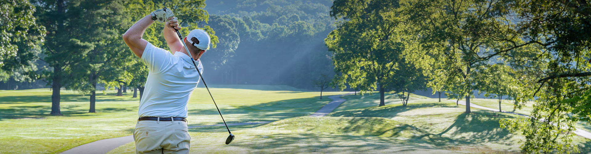 Golfer finishing a tee shot on a tree-lined Springdale fairway