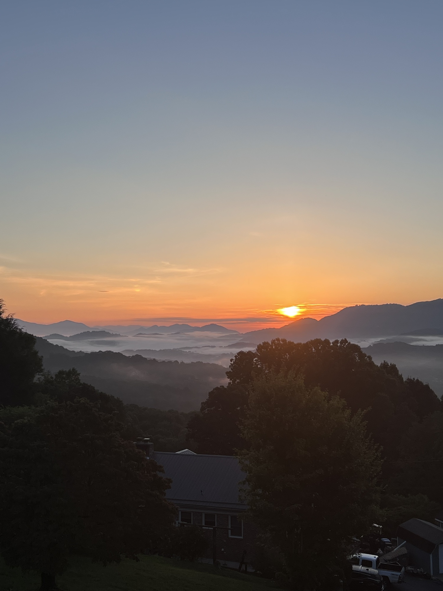 Orange sunrise over layered mountain ridges and morning fog